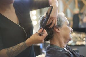 Thợ dùng lược và kéo cắt tóc cho một phụ nữ tóc bạc