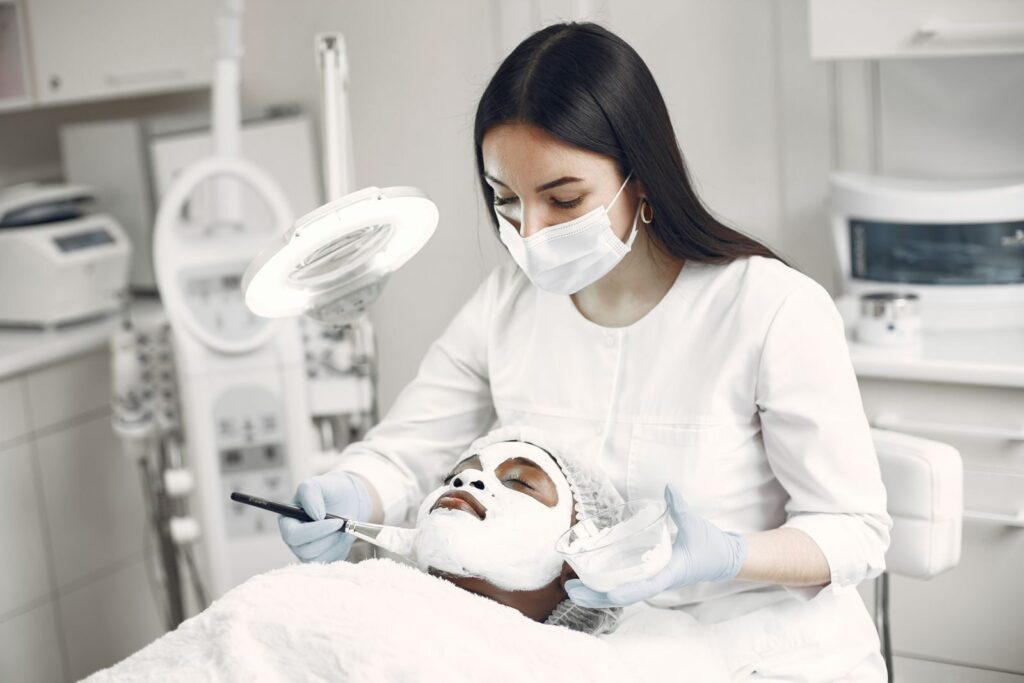 Chuyên viên đeo găng chăm sóc da mặt cho khách dưới đèn tại spa
