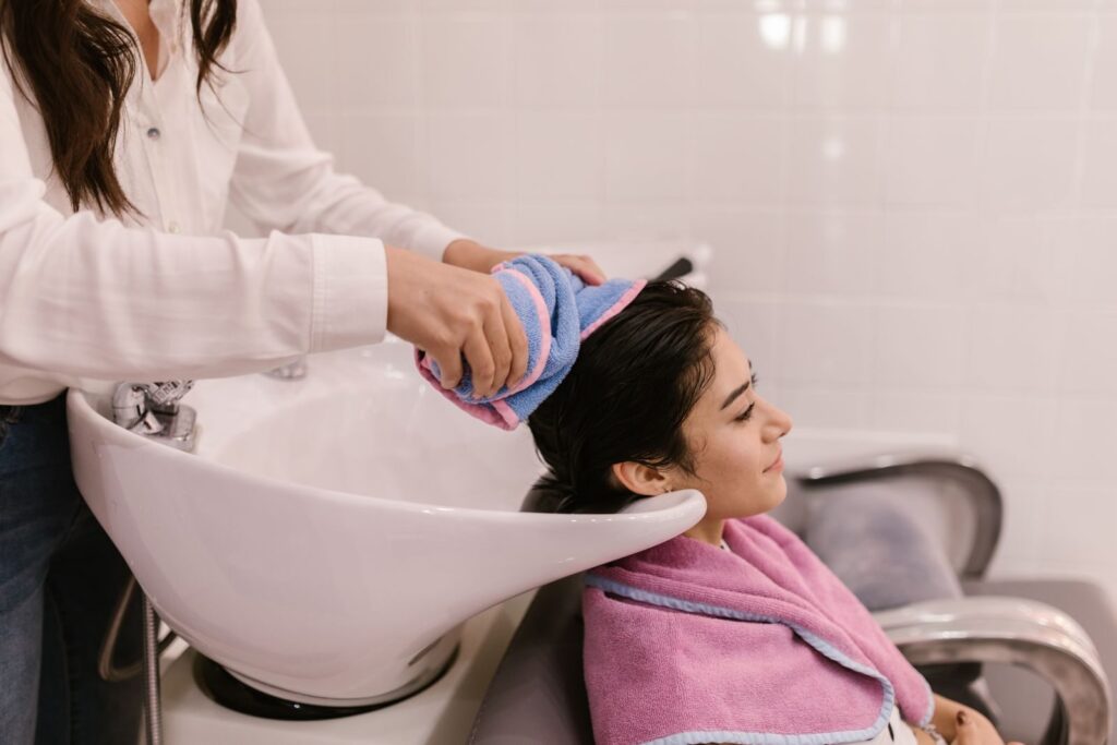 Thợ tóc dùng vòi xả nước lên tóc khách tại bồn gội trong salon