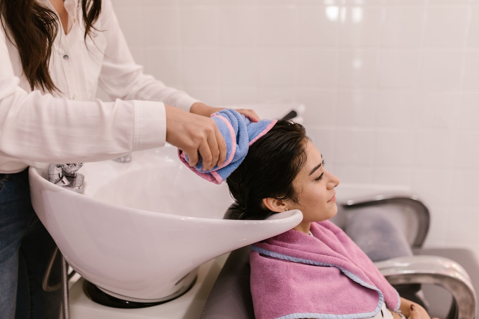 Thợ tóc dùng vòi xả nước lên tóc khách tại bồn gội trong salon