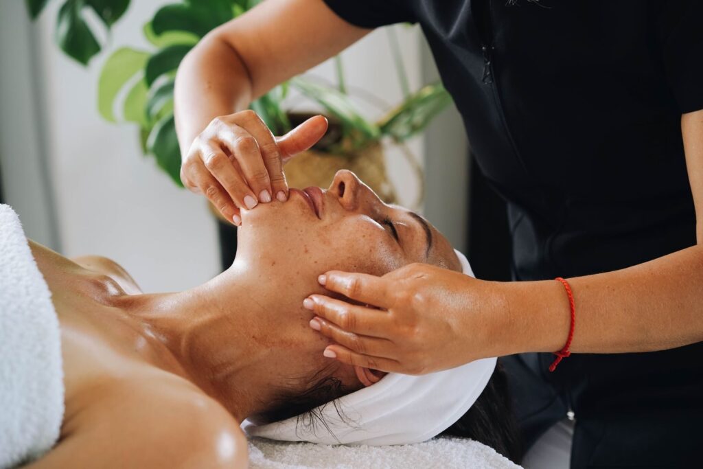 Chuyên viên dùng hai tay massage mặt cho khách nằm trên giường spa