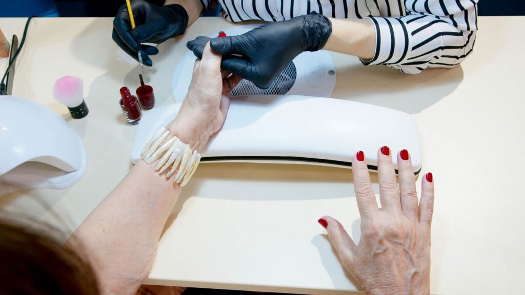 Thợ nail đeo găng chăm sóc móng tại bàn manicure, nhìn từ trên xuống