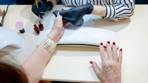 Thợ nail đeo găng chăm sóc móng tại bàn manicure, nhìn từ trên xuống