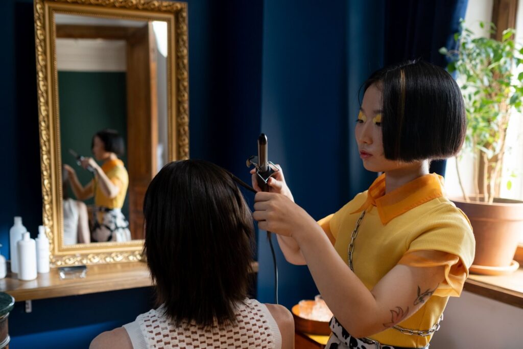 Thợ làm tóc dùng máy uốn tạo kiểu cho khách trước gương salon