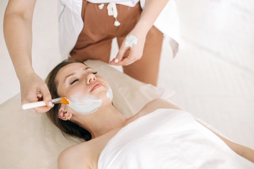 Chuyên viên dùng cọ thoa mặt nạ lên má khách tại spa