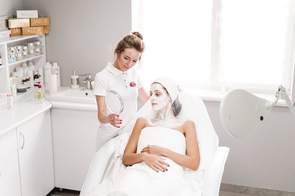 Chuyên viên cầm gương trao đổi với khách đang đắp mặt nạ chăm sóc da