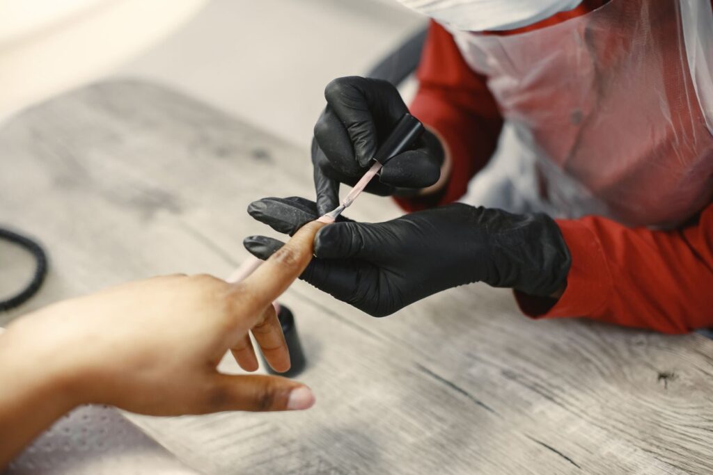 Thợ Nail đeo găng sơn móng cho khách tại bàn làm việc