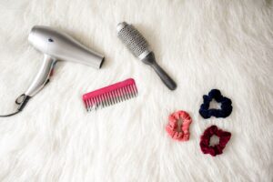 Máy sấy, lược chải, lược hồng và dây buộc tóc đặt trên nền sáng