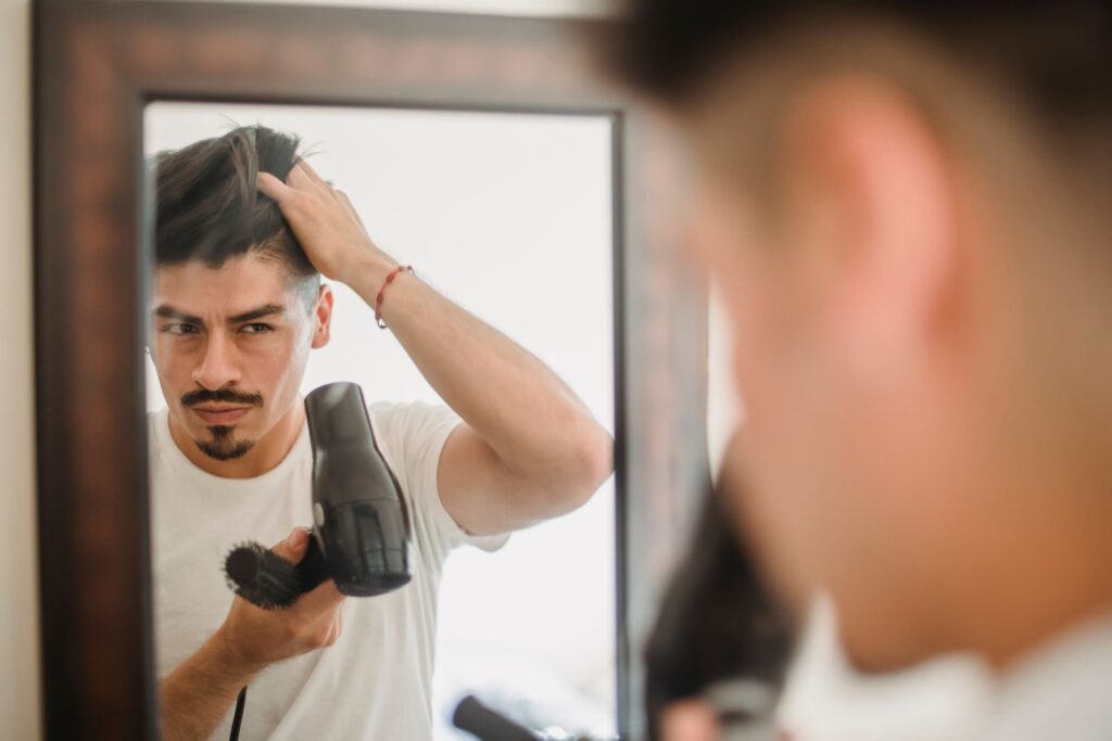 Người đàn ông dùng máy sấy tạo kiểu tóc trước gương