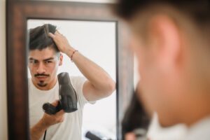 Người đàn ông dùng máy sấy tạo kiểu tóc trước gương