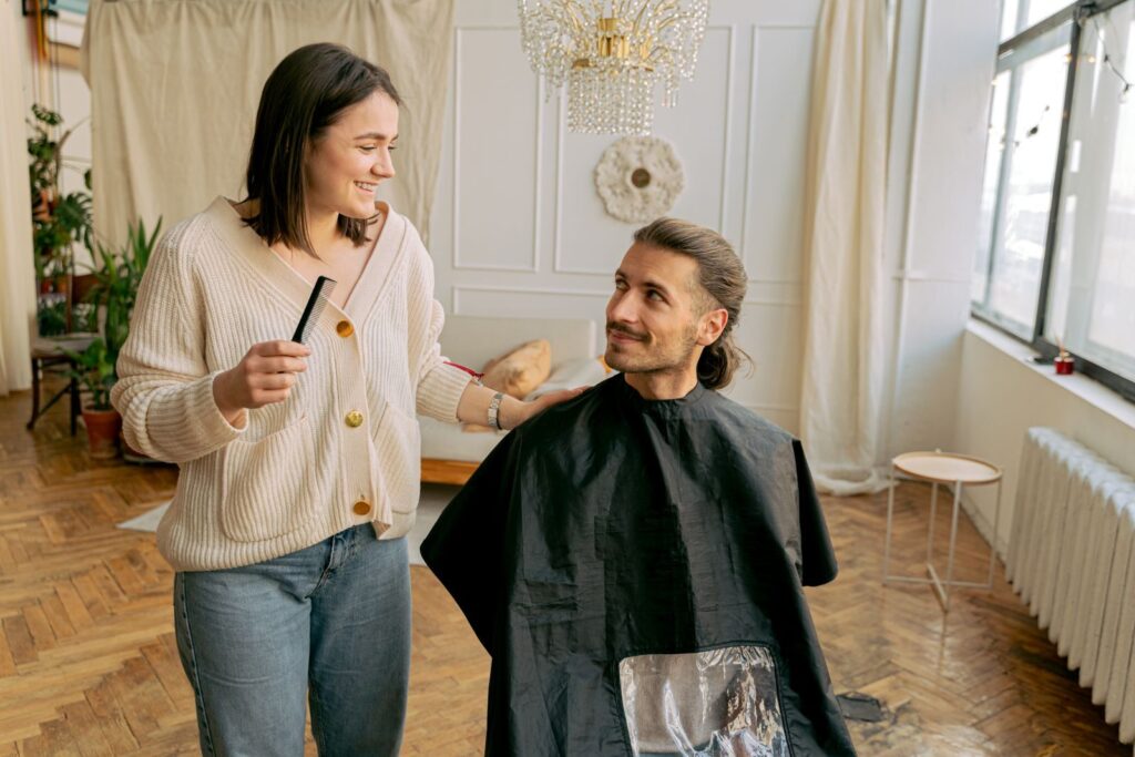 Thợ làm tóc cầm lược và trò chuyện với khách nam ngồi trên ghế salon