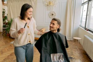 Thợ làm tóc cầm lược và trò chuyện với khách nam ngồi trên ghế salon