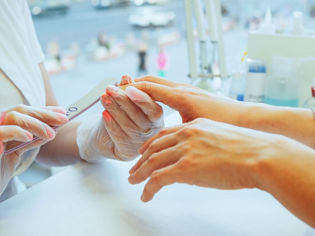 Thợ nail dùng dũa chăm sóc móng tay khách tại salon
